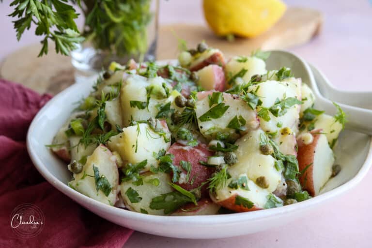 lemon caper potato salad with parsley and lemons in white bowl