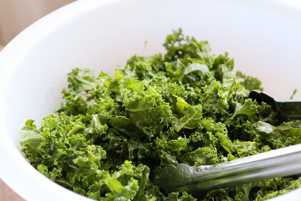 kale in white plastic bowl with tongs 