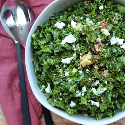 sweet kale quinoa salad in white bowl with serving spoons