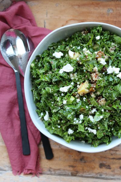 sweet kale quinoa salad in white bowl with serving spoons