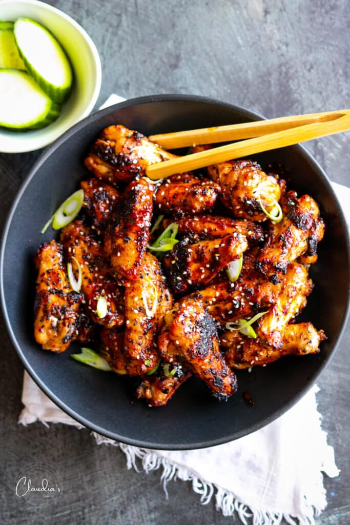 spicy grilled Asian style chicken wings in black bowl with bamboo tongs