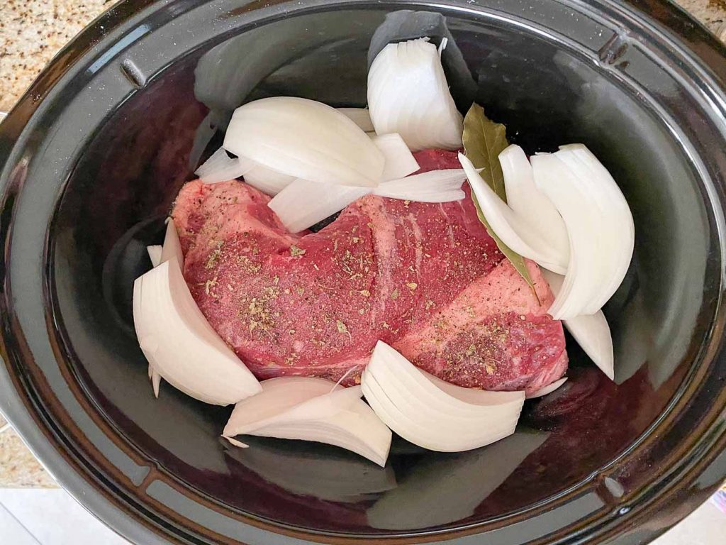 raw brisket in slow cooker with onions and spices