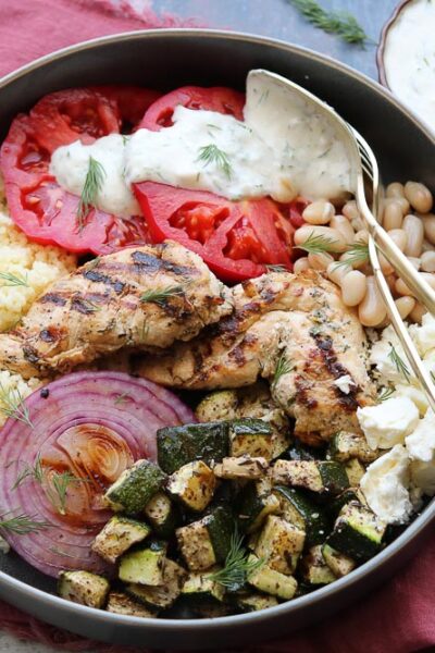 Mediterranean Grilled Chicken bowl with Yogurt Dill Dressing in bowl with napkin and extra dressing on the side.