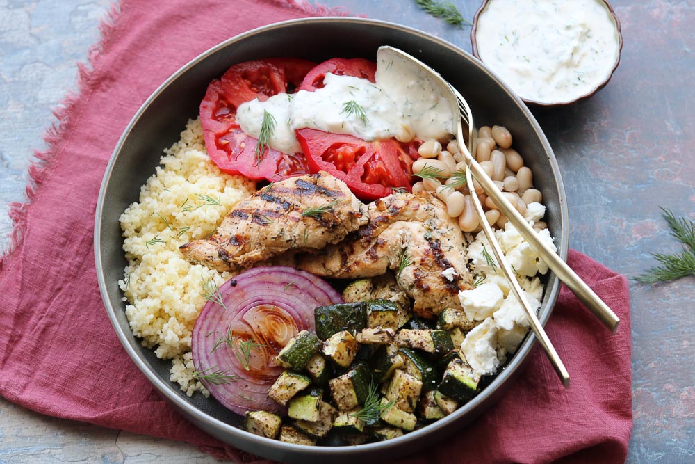 mediterranean grilled chicken bowl with fork on table with napkin and yogurt dill dressing
