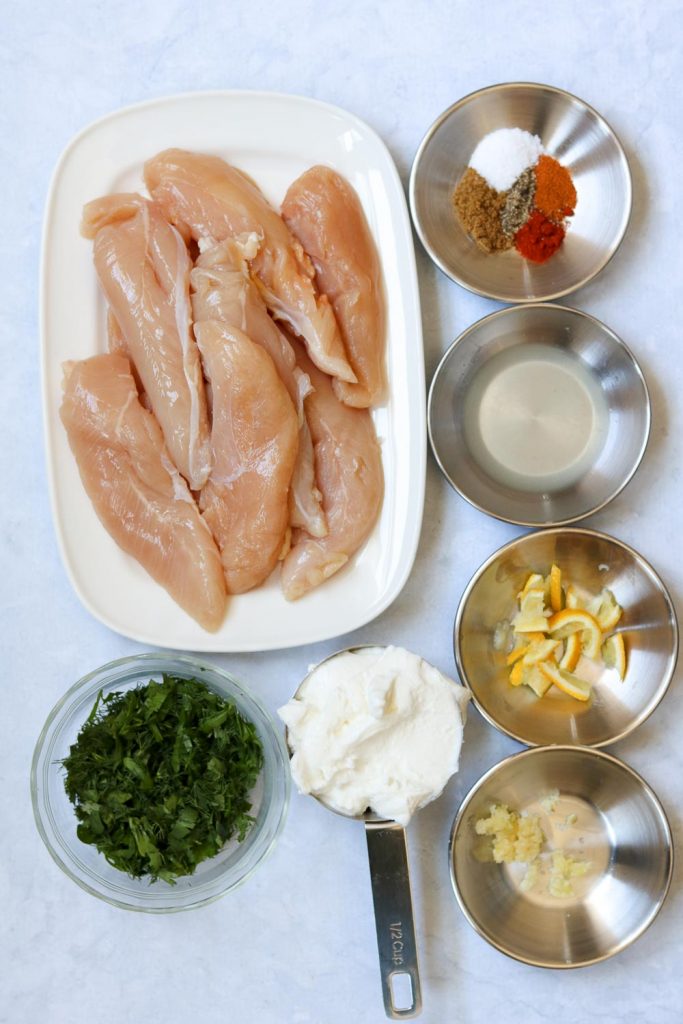 raw chicken on plate with ingredients for yogurt herb marinated grilled chicken
