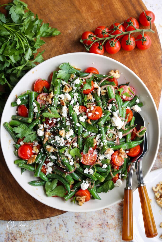 cold green bean salad in bowl with ingredients around it. 