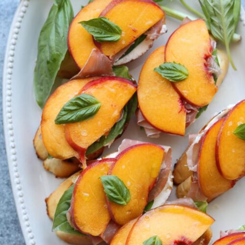 peach prosciutto mascarpone crostini on platter with basil