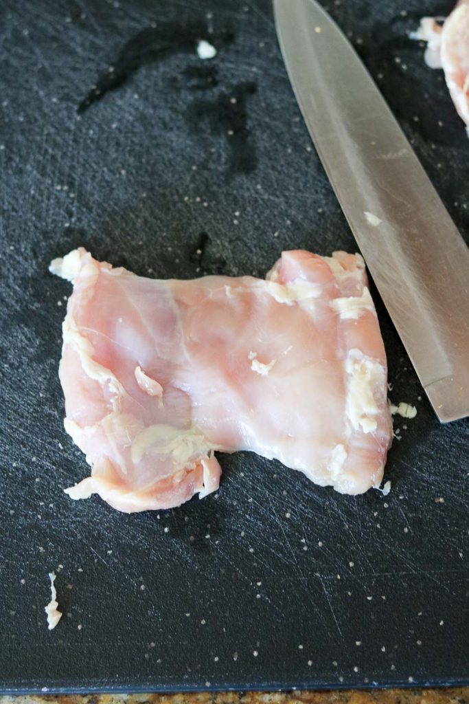 trimmed chicken thigh on cutting board with knife