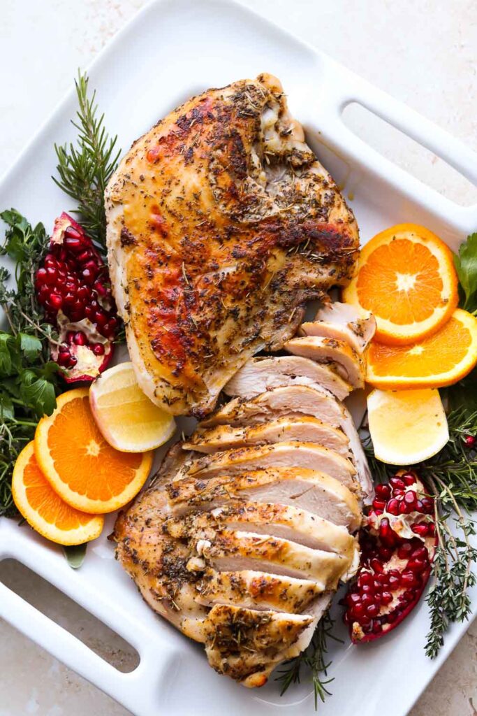turkey on white platter with orange and fresh herbs