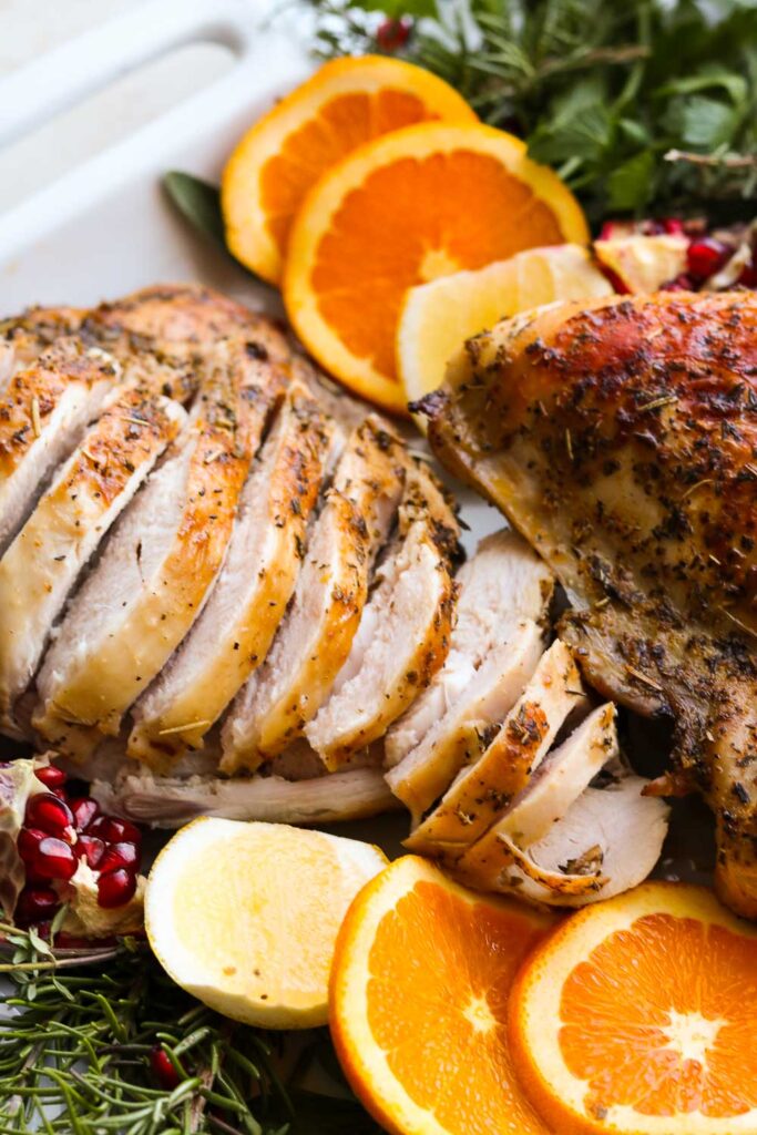 oven roasted herbed turkey breast on platter with herbs and citrus