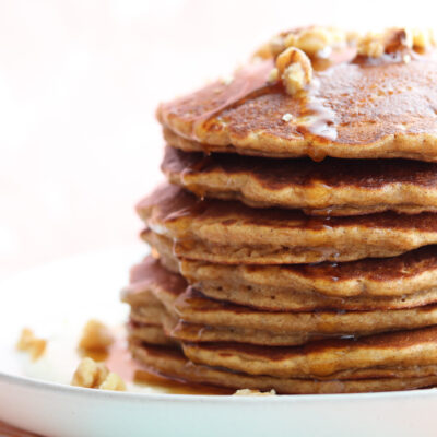 horizontal photo of stack of coconut carrot cake pancakes with cream cheese sauce