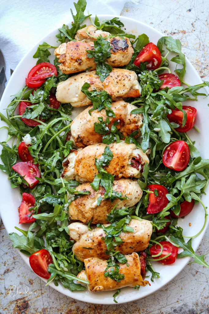 grilled chicken involtini with arugula salad on white platter 