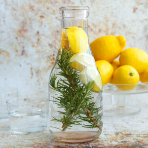 square image of rosemary lemon water with lemons in the background in clear carafe