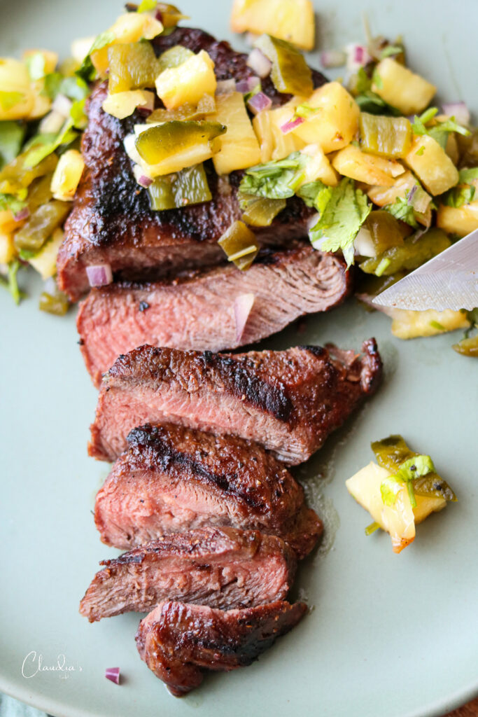 ancho Chile rubbed steak with grilled pineapple salsa on green plate with knife