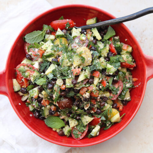 chopped salad in red bowl with black serving spoon