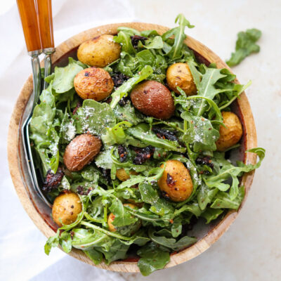 arugula with potatoes in bowl with serving utensils