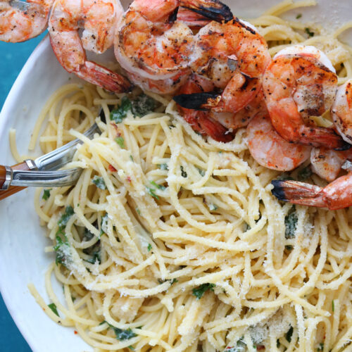 roasted garlic and shrimp spaghetti in white bowl with shrimp on skewers