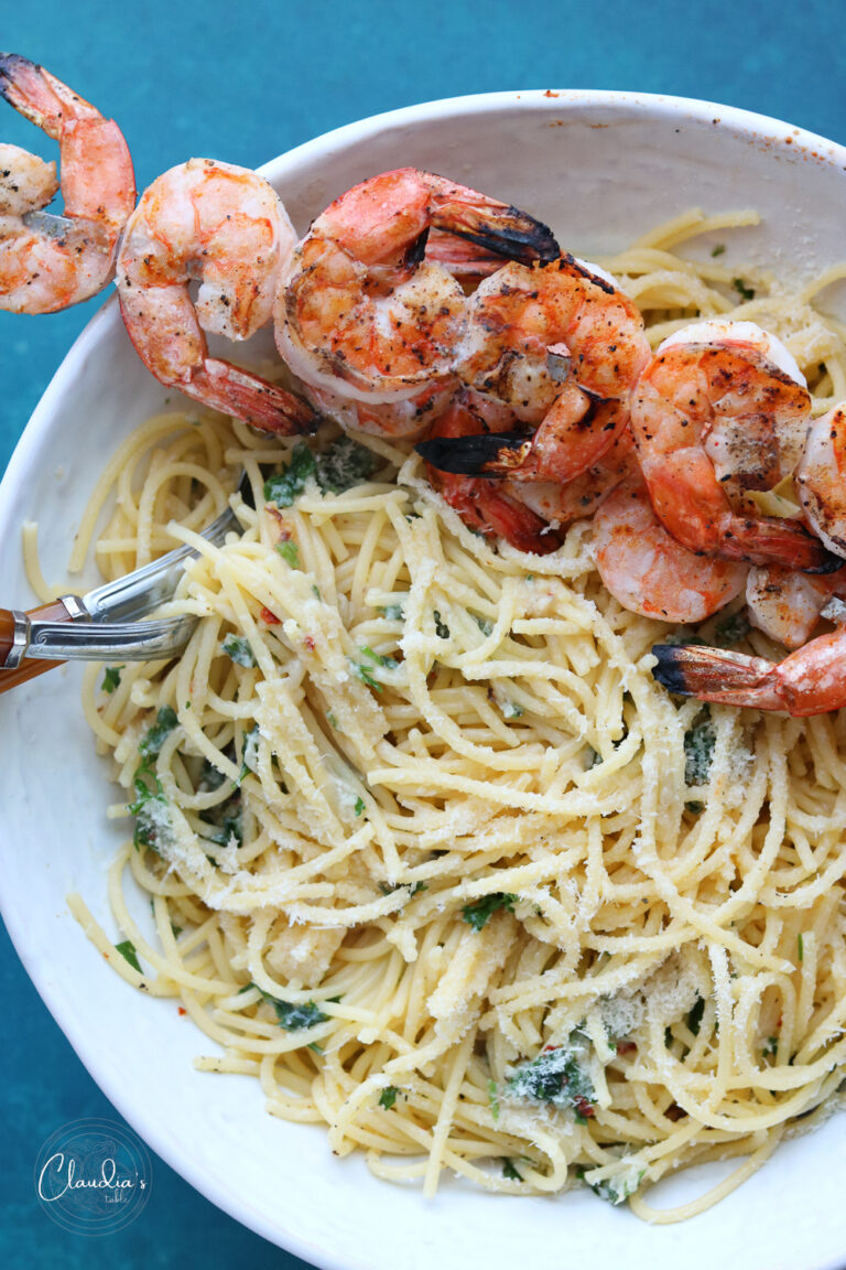 roasted garlic and shrimp spaghetti in white bowl with shrimp on skewers