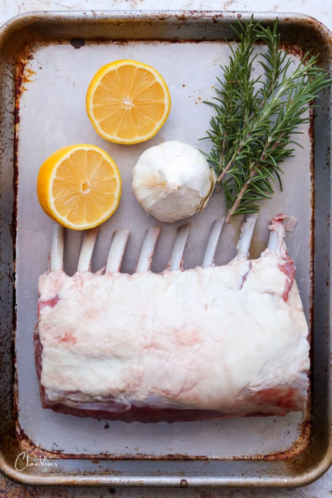 uncooked rack of lamb on baking sheet with lemon, garlic and rosemary 