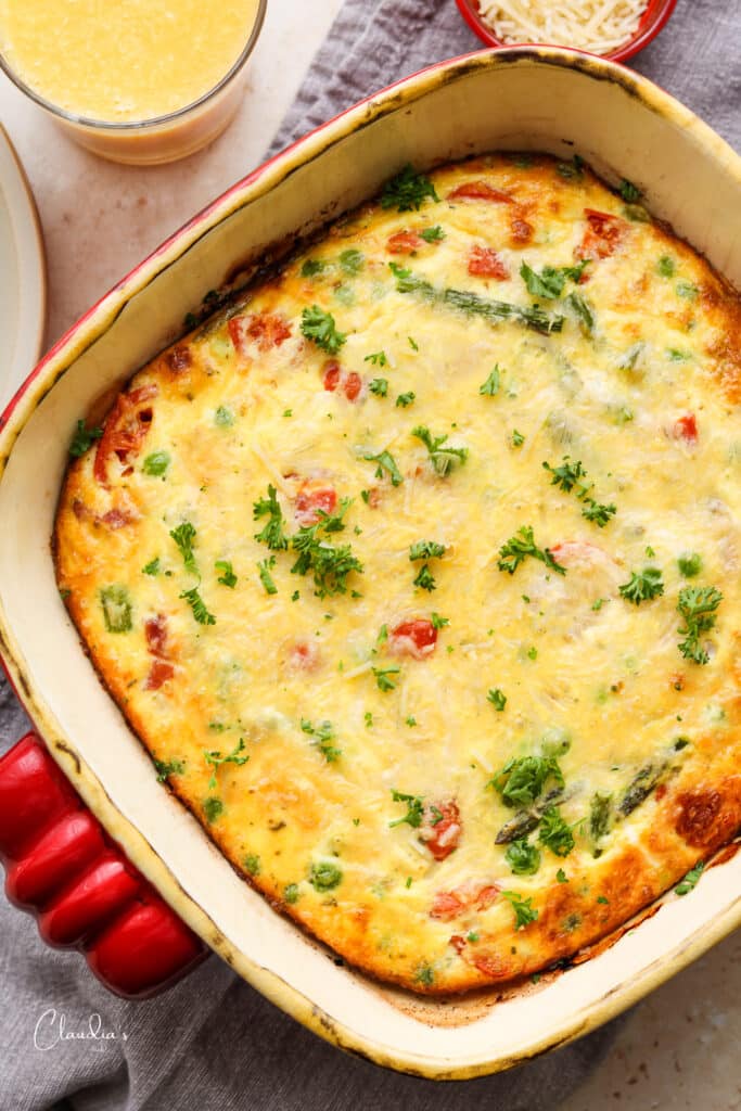 asparagus frittata in red baking dish with a glass of orange juice