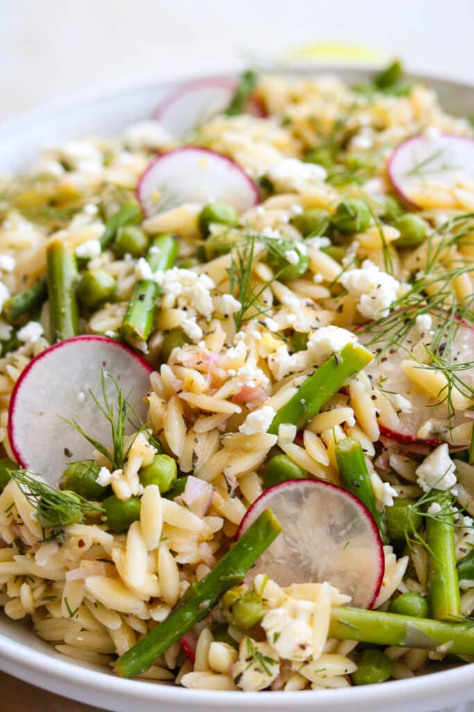 orzo salad with asparagus and peas in white bowl with lemons in the background