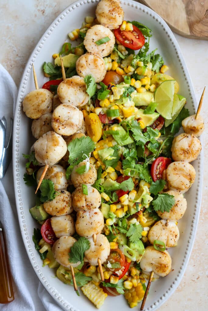 grilled scallops with corn and avocado salad on white platter 
