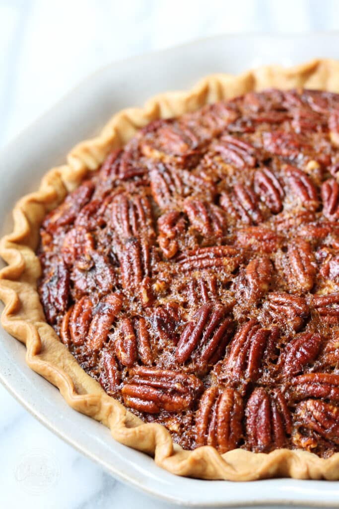 Brown butter Bourbon pecan pie close up in white pie dish on white background 