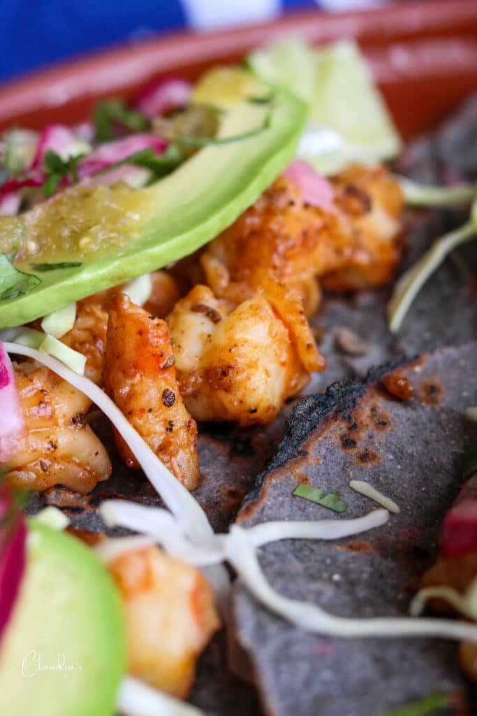 top spicy shrimp tacos with shredded cabbage, pickled red onions, green chile salsa and avocado 