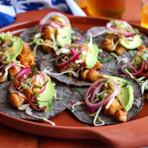 platter of spicy shrimp tacos with pickled onions, avocado, salsa and cabbage