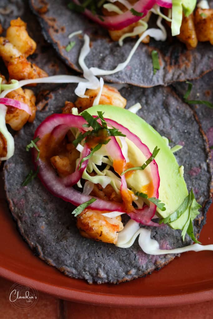 close up of spicy shrimp tacos with avocado, pickled onions, green salsa, and cabbage