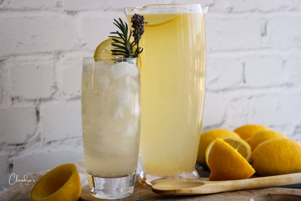 Lavender lemonade in tall glass with lemons on the side