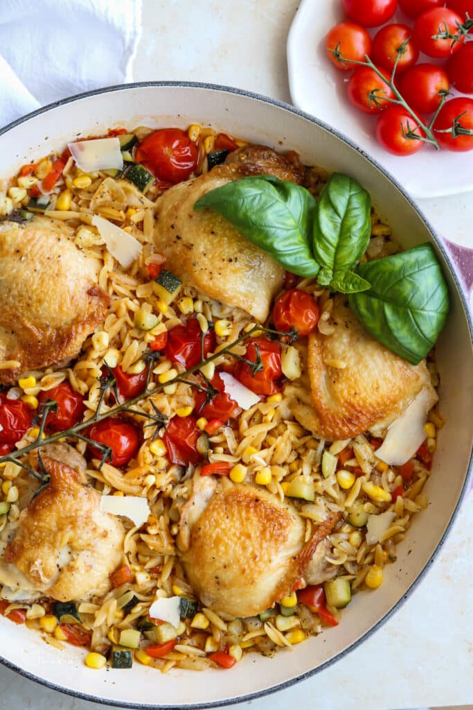 chicken with summer vegetable orzo in le creuset garnished with fresh basil 