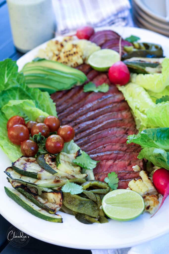 close up grilled steak salad with corn, zucchini , tomatoes, peppers, radish and avocado