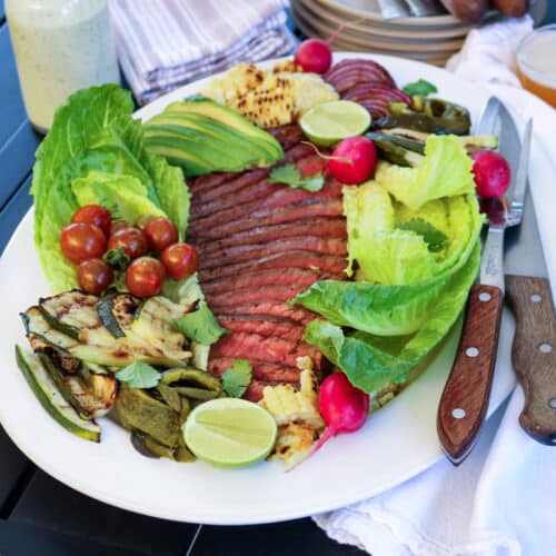 grilled steak salad on white platter served with beer.