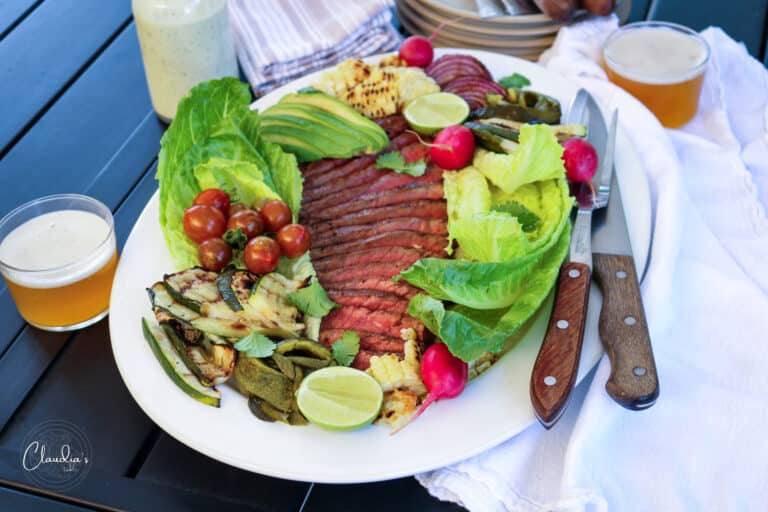 grilled steak salad on white platter served with beer.