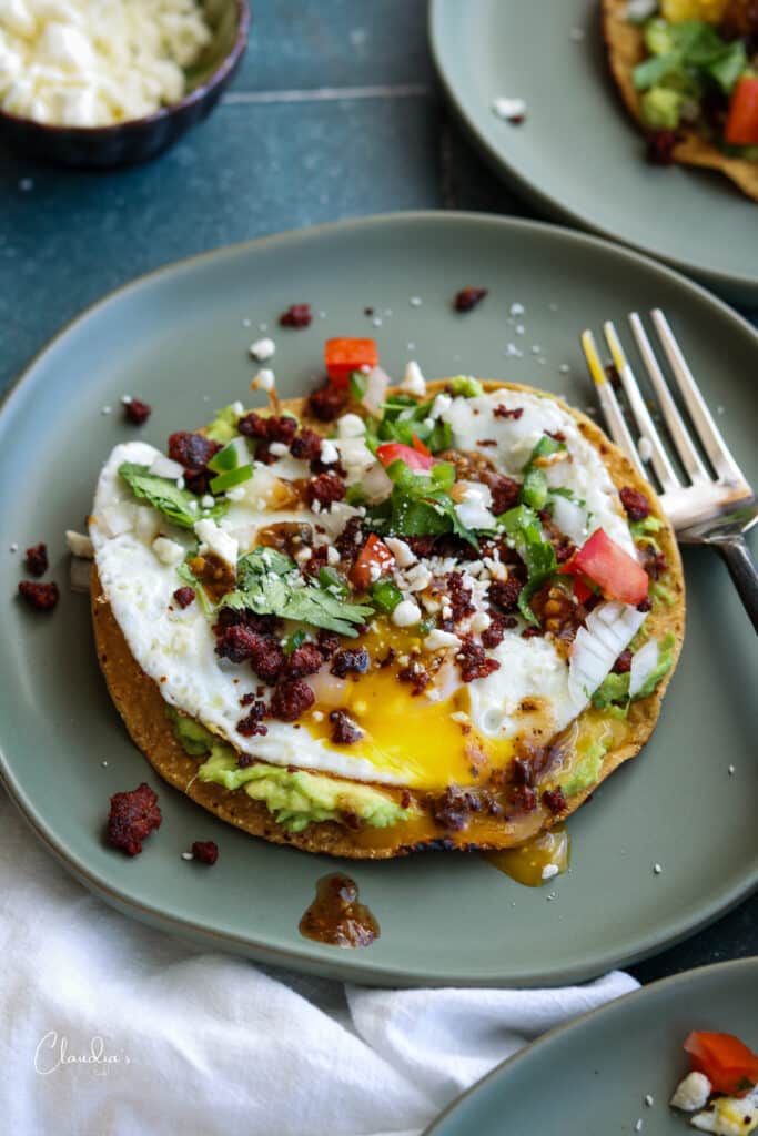 breakfast tostada with avocado, egg, pico de Gallo on a green plate.