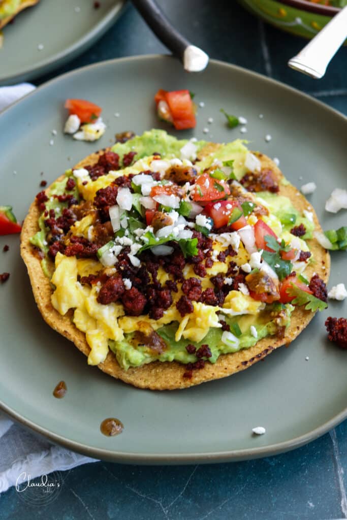 breakfast tostada with avocado, eggs and chorizo atop of crispy tostada shell. 