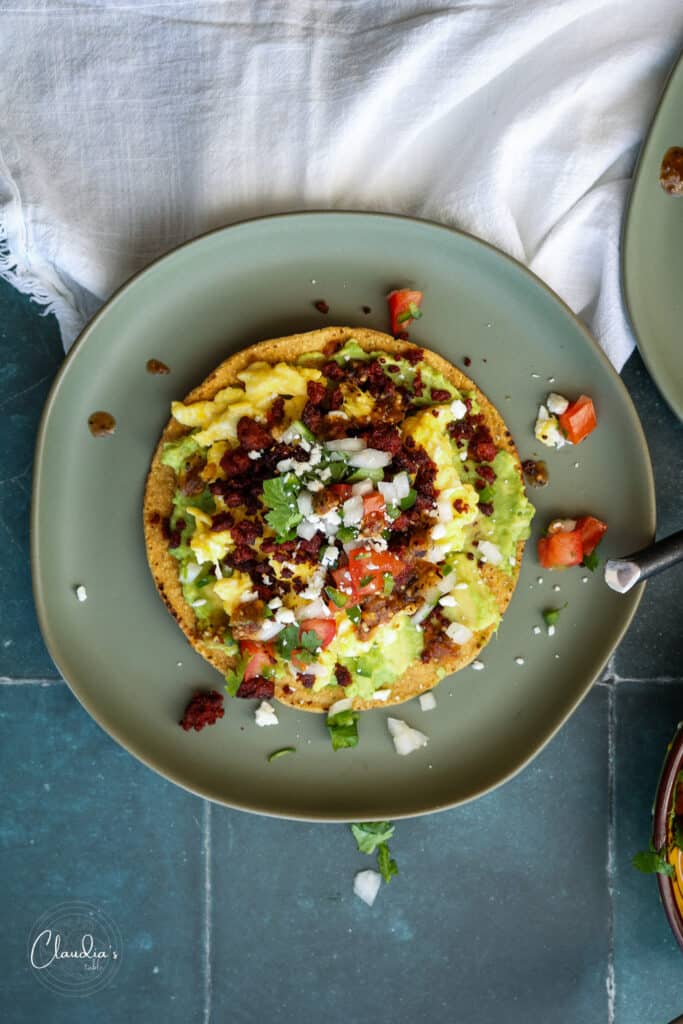 breakfast tostada with chorizo with scrambled eggs on green plate with pico de gallo. 