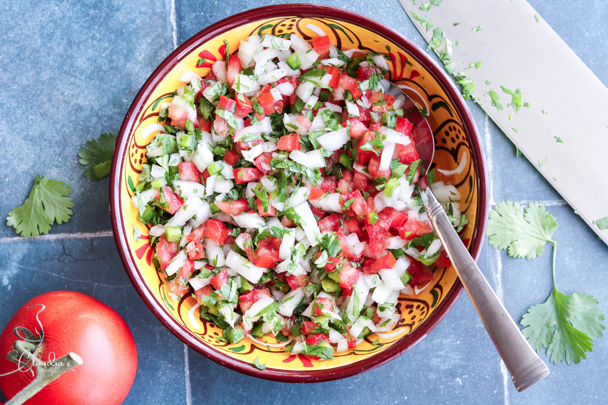 horizonal image of fresh pico de Gallo in colorful bowl with tomatoes on the side