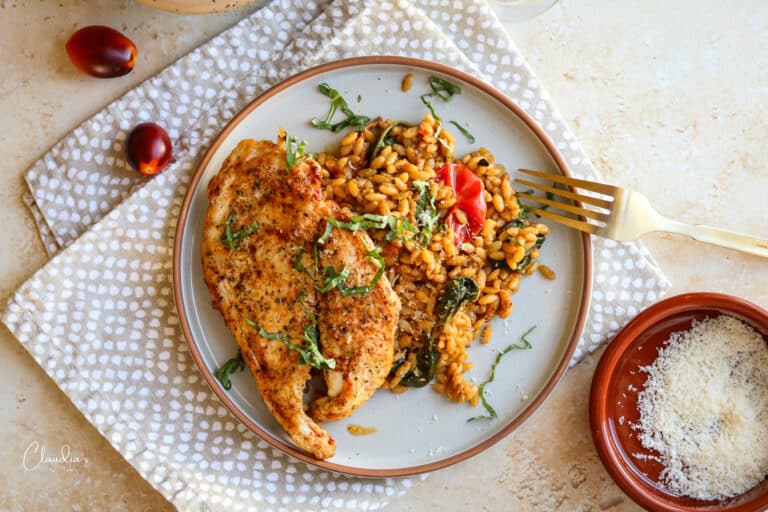 chicken cutlets with creamy tomato orzo plated on beige plates and garnished with basil and parmesan cheese