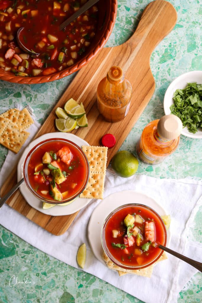 top view of Mexican Shrimp Cocktail with hot sauce, lime wedges and crackers. 