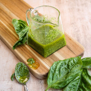 basil pesto vinagirette in small glass mini pitcher with fresh basil on the side.