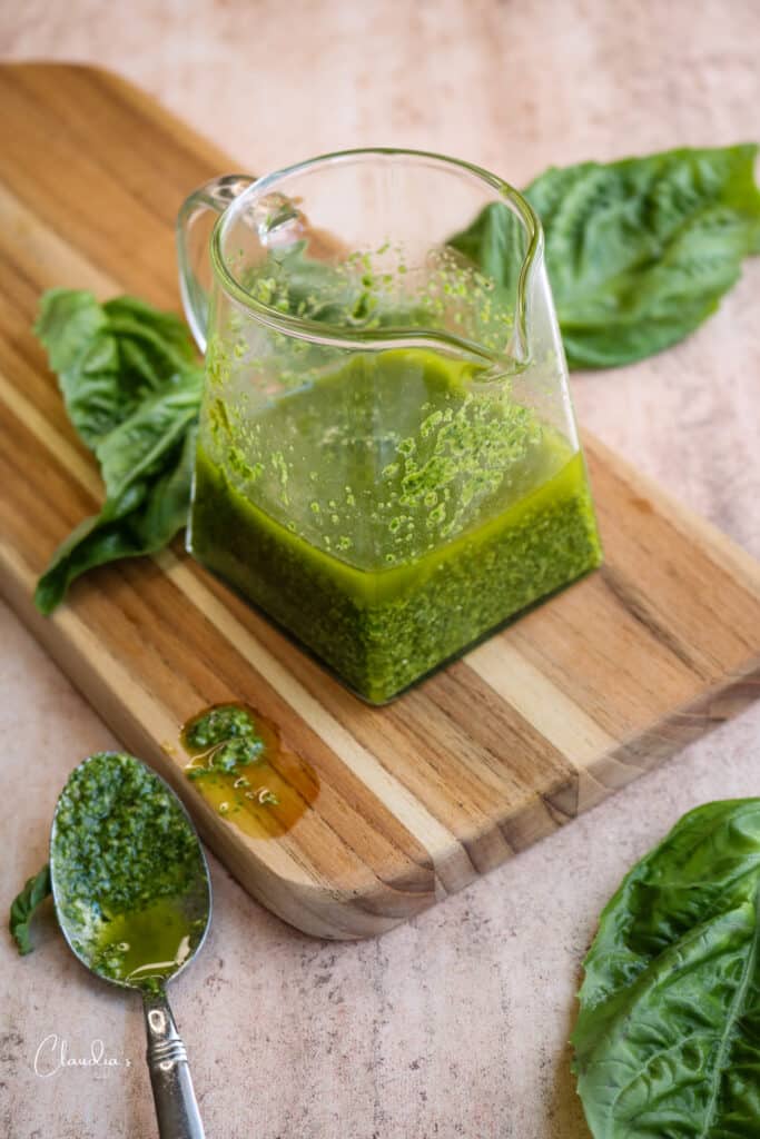 simple basil pesto vinaigrette in glass pitcher with fresh basil leaves around it.